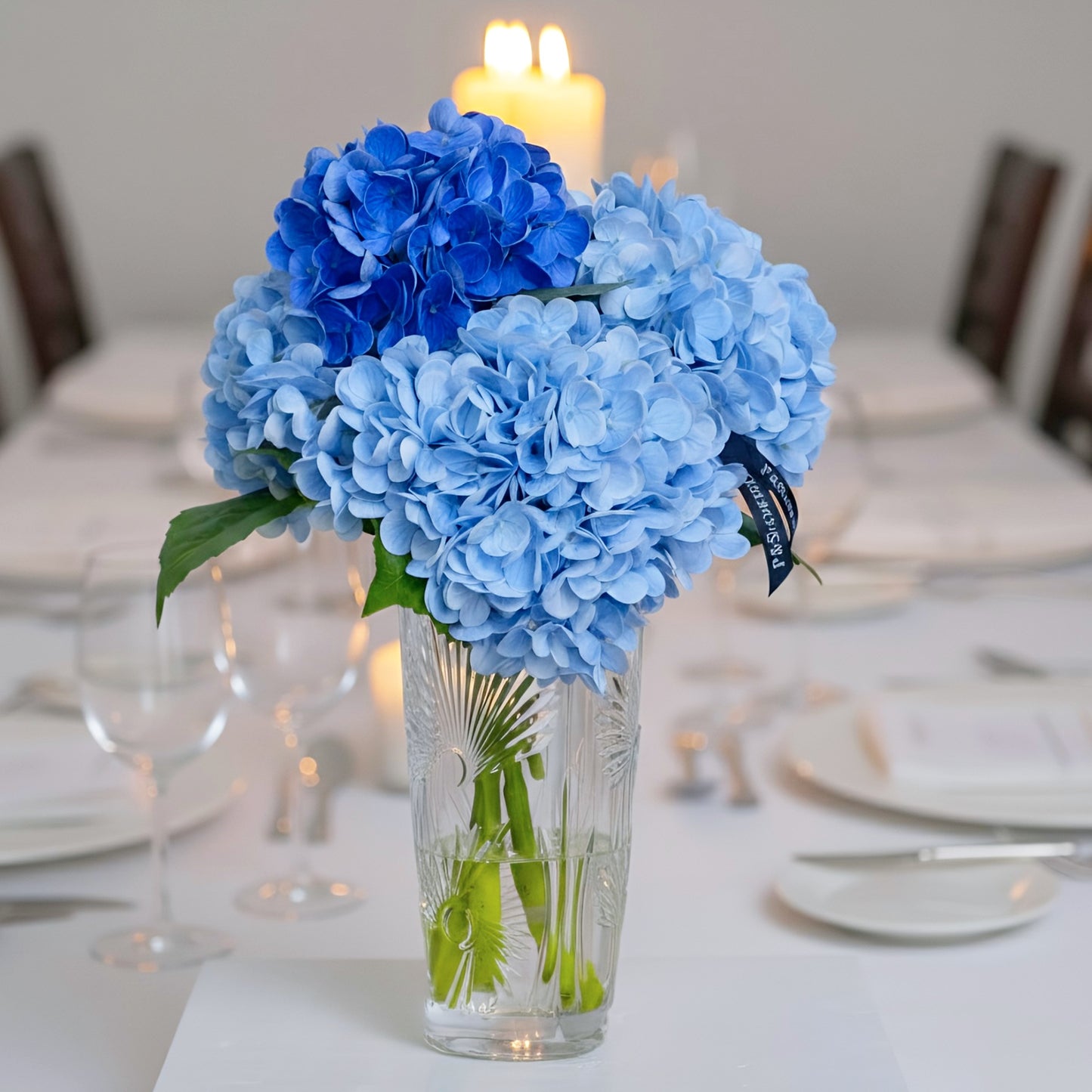 Bouquet of blue hydrangeas in a clear vase on a decorated table with candles.