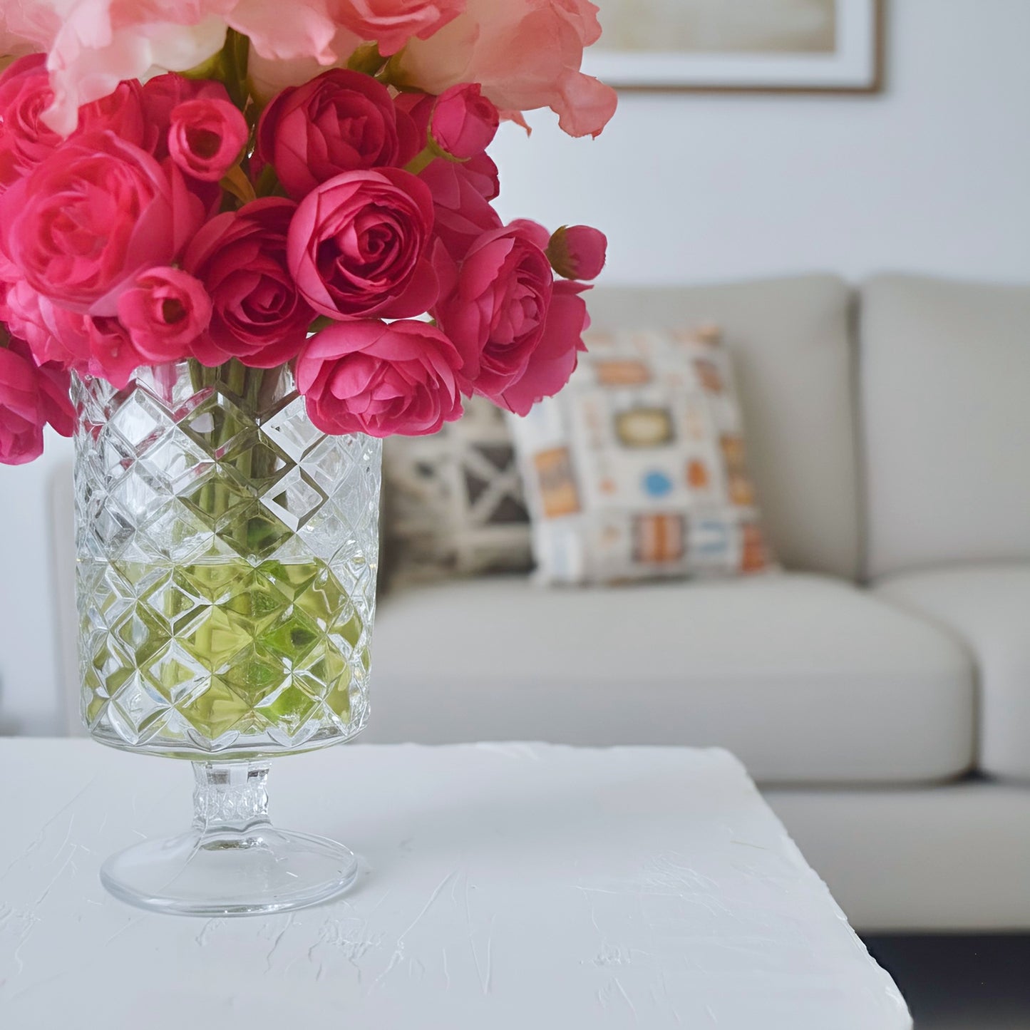 Bouquet of pink roses in a clear glass vase on a table with a sofa and cushions in the background.