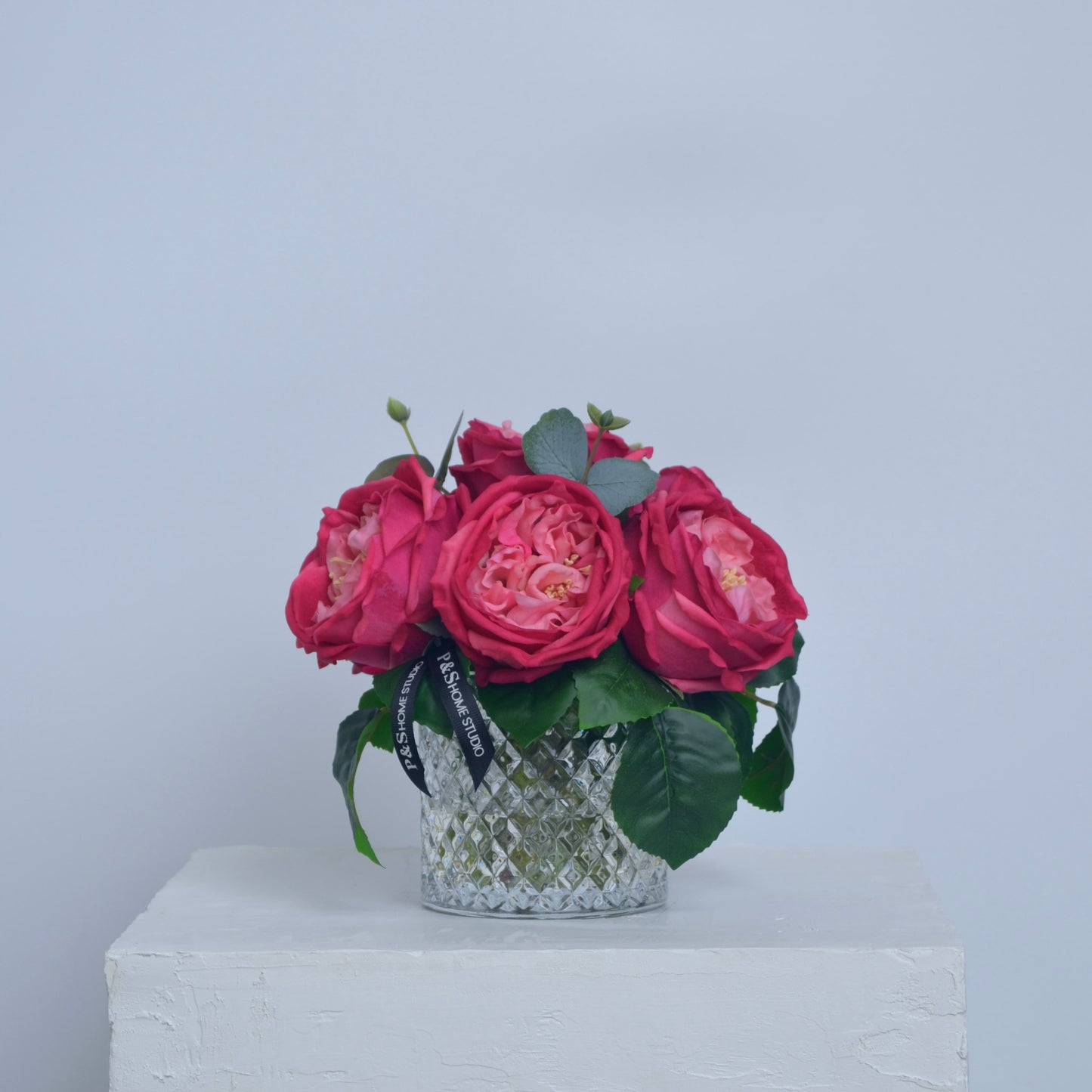 Bouquet of pink flowers in a decorative vase on a white surface with a light blue background