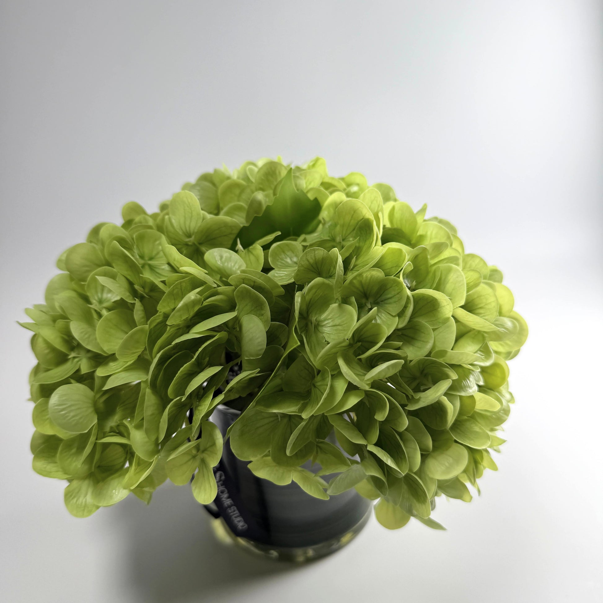 Green artificial flower ball on a white background. Green hydrangea in glass vase faux floral