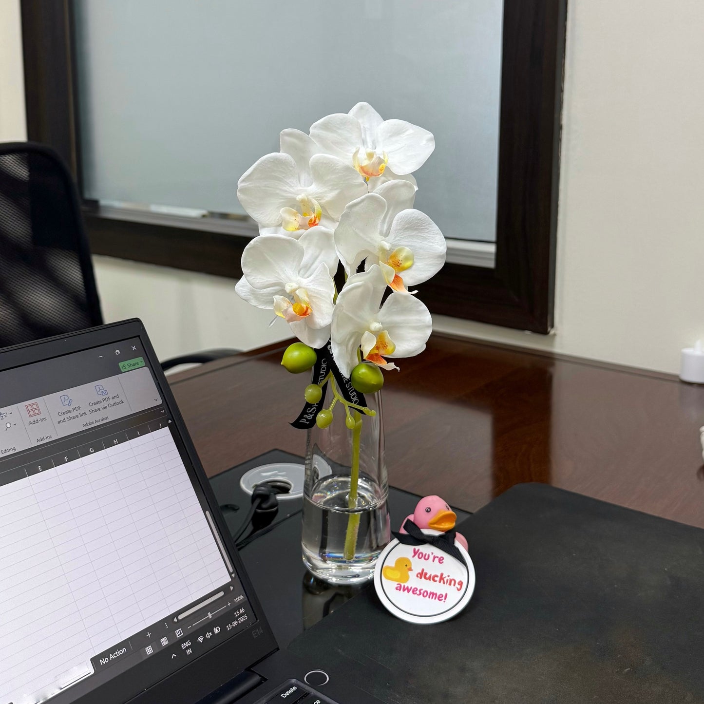 Laptop on a desk with a vase of white flowers and a decorative duck sticker.