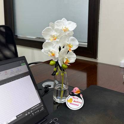 Laptop on a desk with a vase of white flowers and a decorative duck sticker.