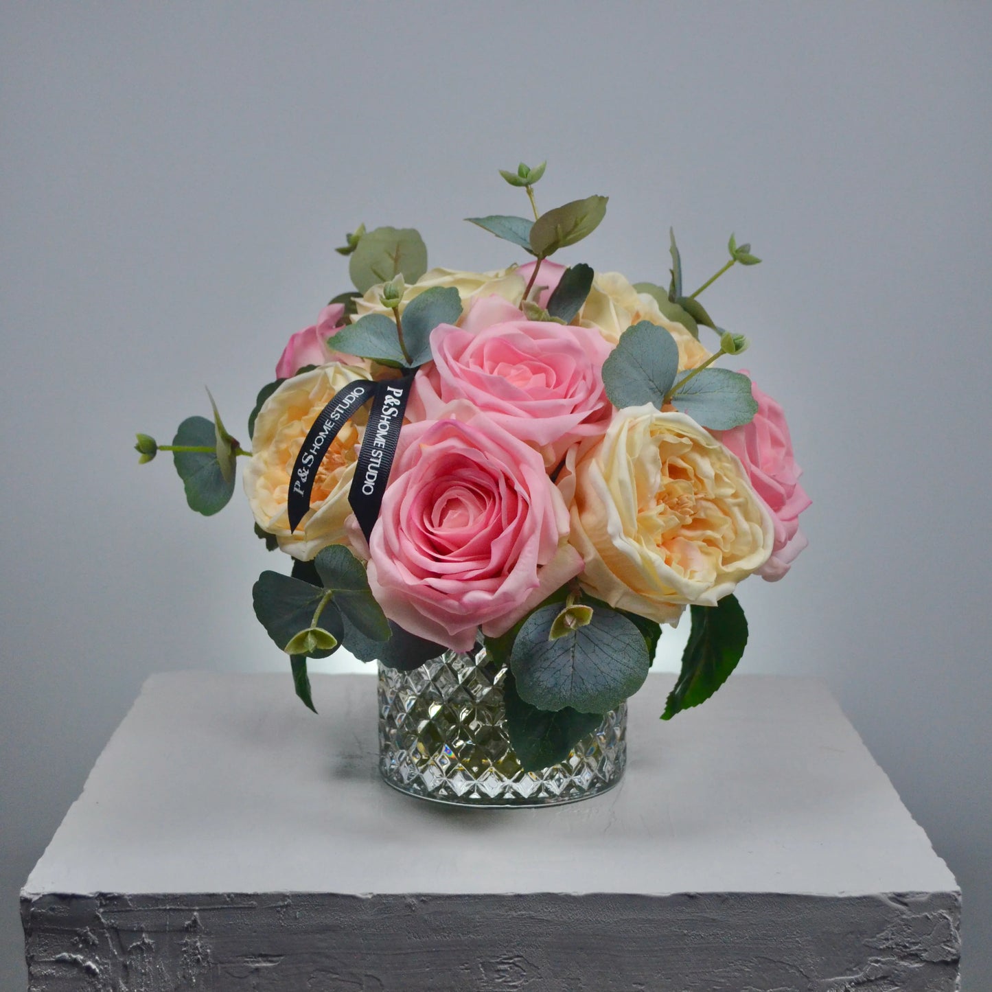 Bouquet of pink and yellow roses with greenery in a clear glass vase on a gray background
