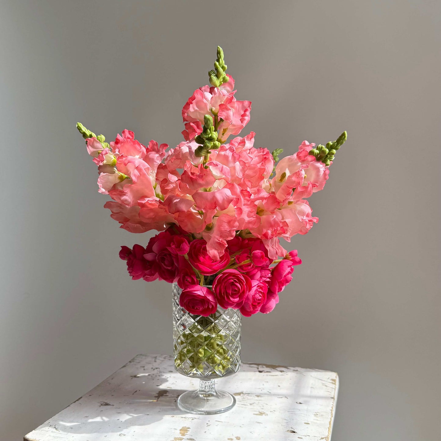 Bouquet of pink and red flowers in a clear glass vase on a wooden surface with a neutral background