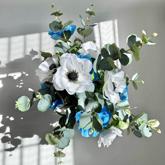 Bouquet of white and blue flowers with green leaves on a gray background
