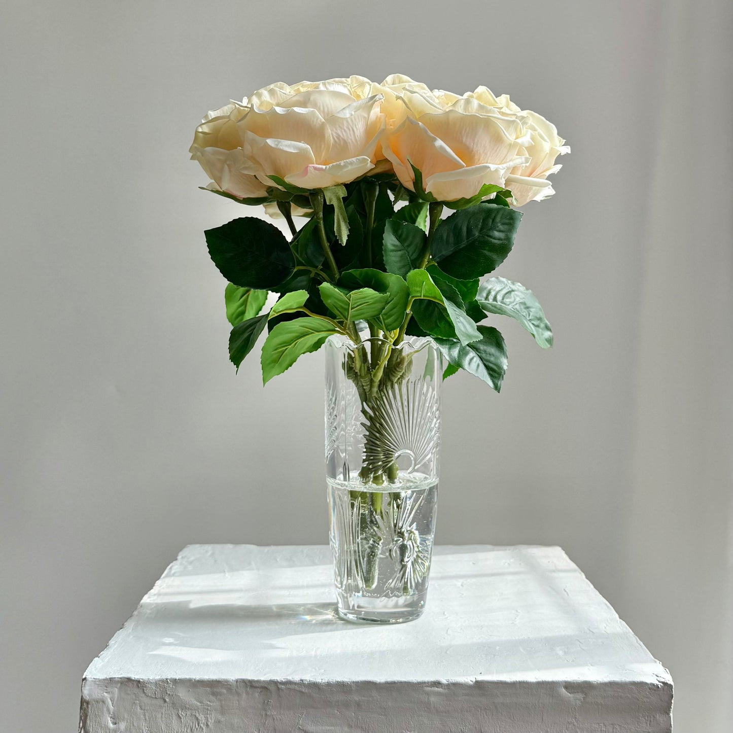 Clear glass vase with beige roses on a white surface against a gray background
