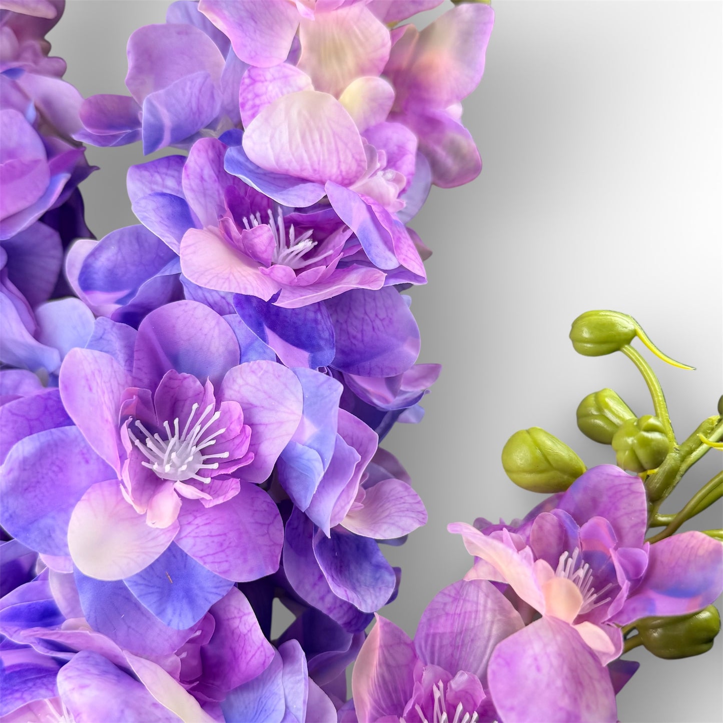 Close-up of purple and pink artificial flowers with green stems on a light gray background
