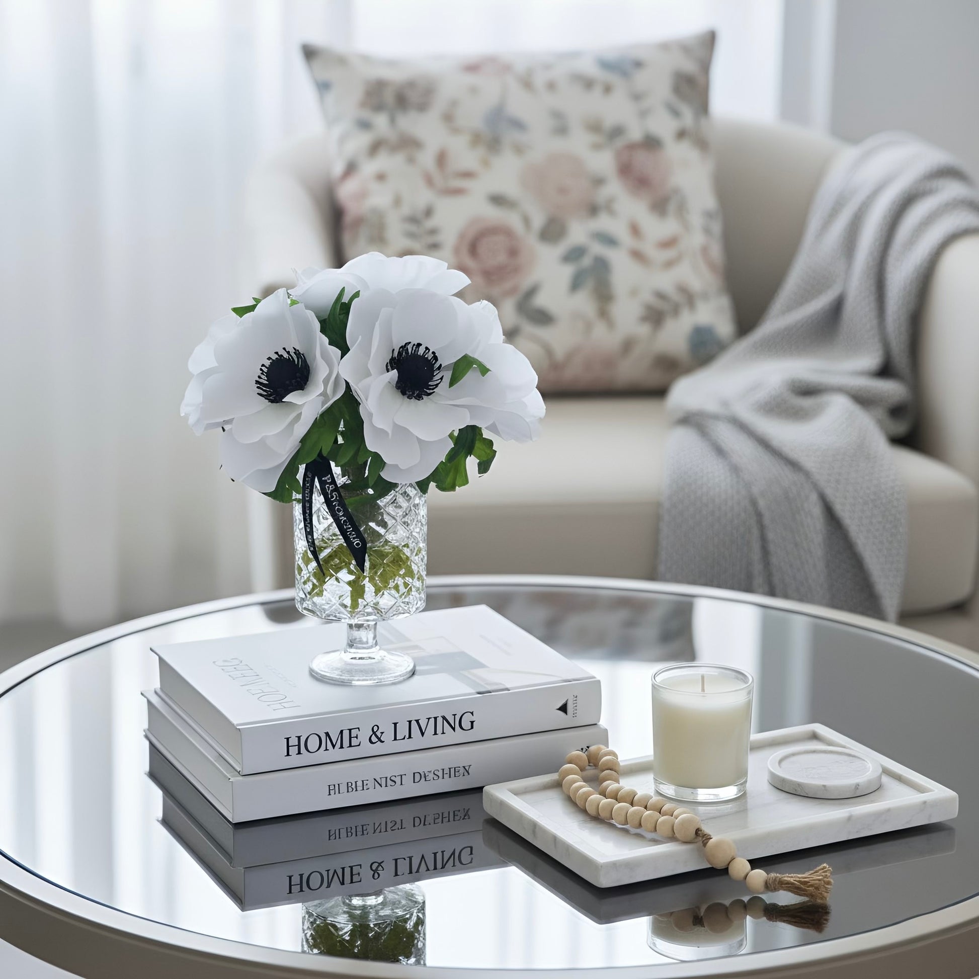 Decorative setup on a glass coffee table with books, flowers, and a candle.