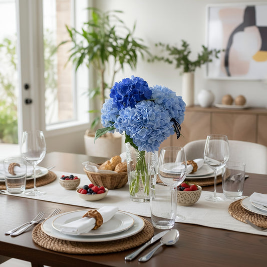 Dining table set with blue flowers, glasses, and food in a bright room.