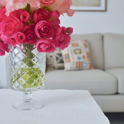 Bouquet of pink roses in a clear glass vase on a table with a sofa and cushions in the background.