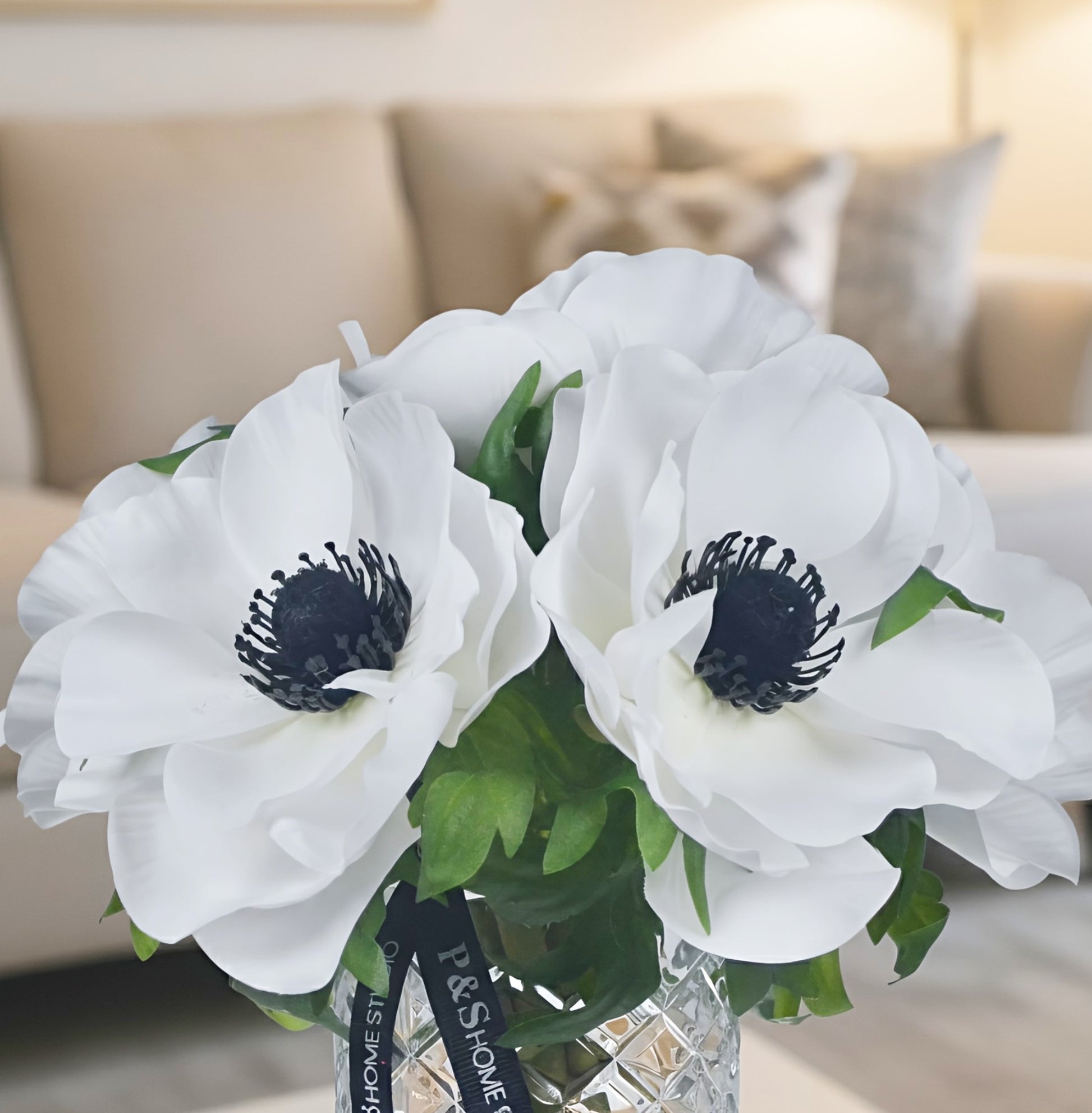 Bouquet of white flowers with black centers in a clear vase on a blurred background