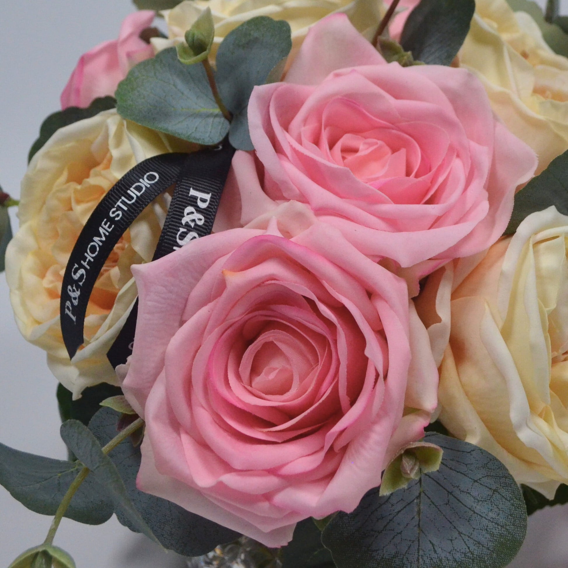 Bouquet of pink and yellow roses with a visible brand label on a light gray background
