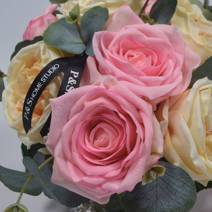 Bouquet of pink and yellow roses with a visible brand label on a light gray background
