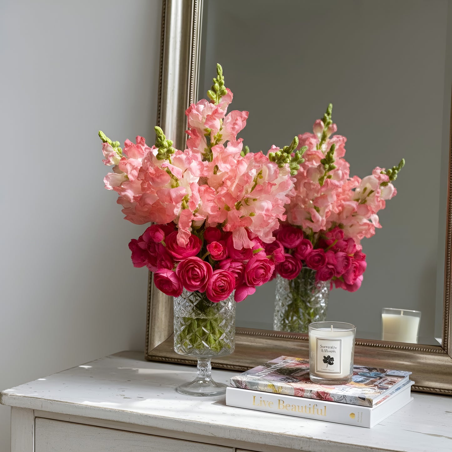 Bouquet of pink and red flowers in a vase on a table with a candle and book.