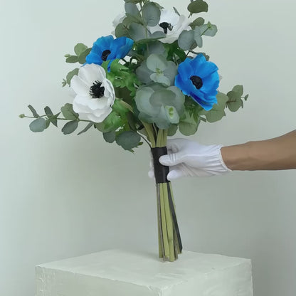 Bouquet of blue and white flowers in a white vase on a surface with books and a light in the background.
